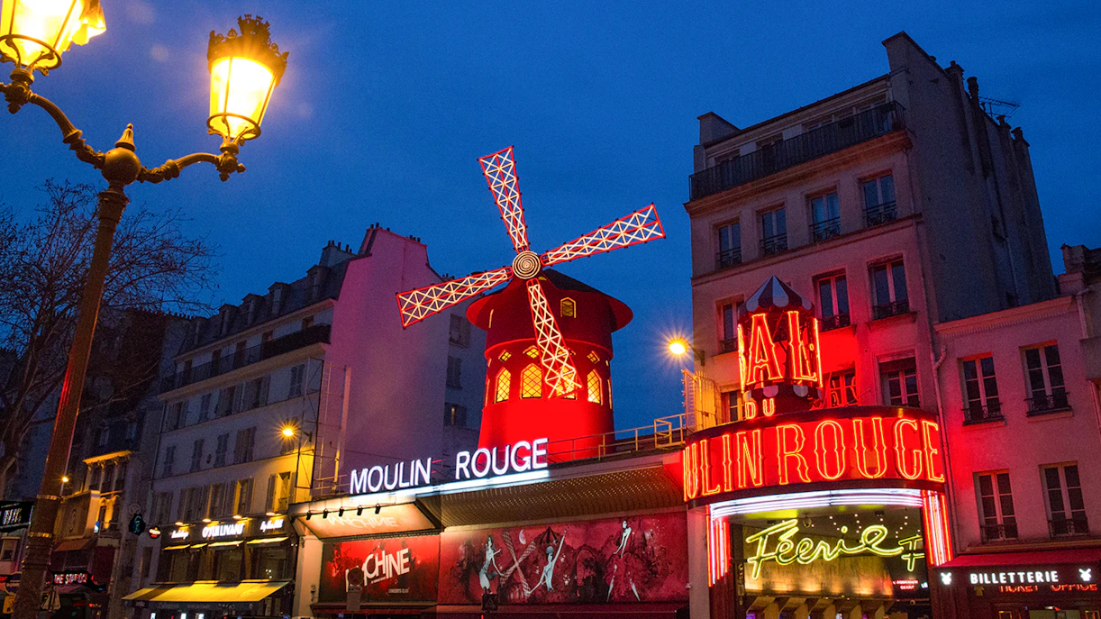 Moulin Rouge in Paris with illuminated windmill and neon signs at night.
