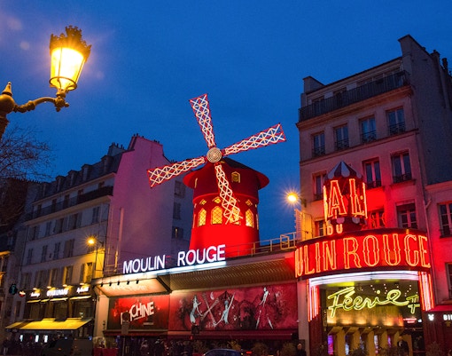 Moulin Rouge in Paris with illuminated windmill and neon signs at night.