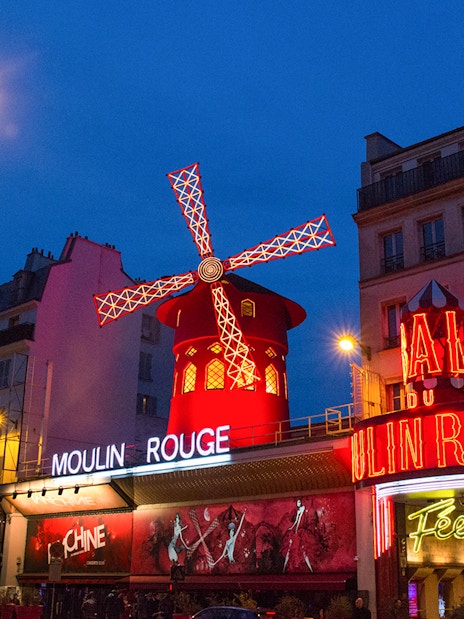 Moulin Rouge in Paris with illuminated windmill and neon signs at night.