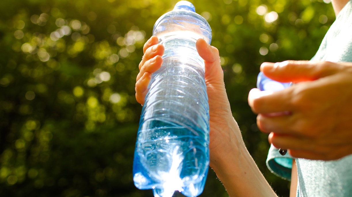 Person holding a water bottle outdoors in sunlight.
