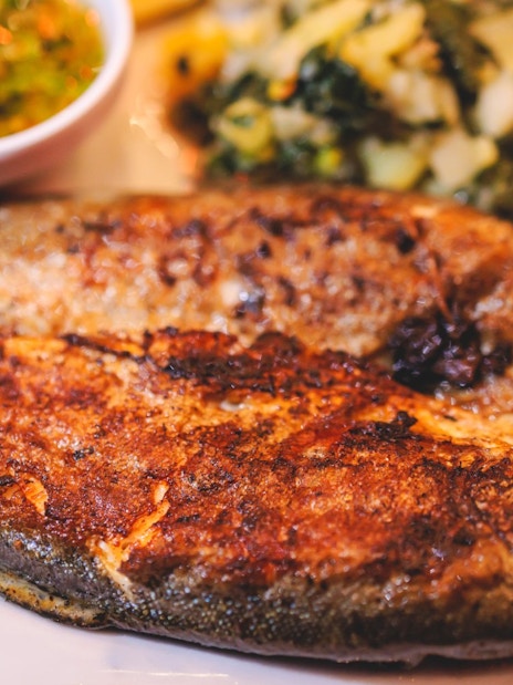 Grilled fish with sauce and vegetables on a plate.