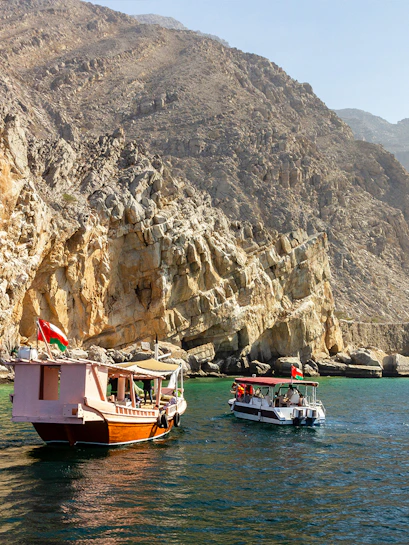 Tourists on dhow boats near rocky cliffs in Khasab, Oman.