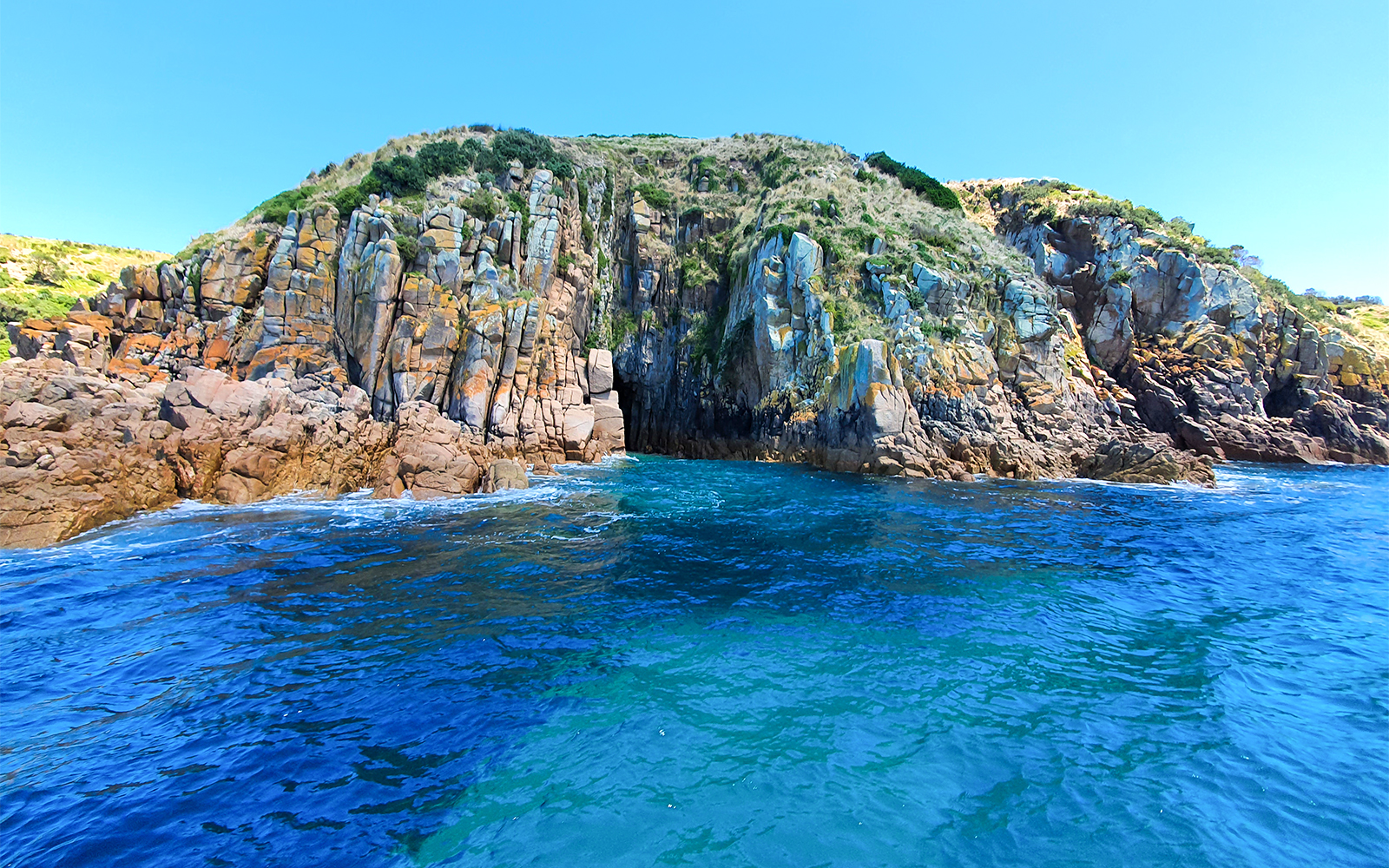 Cruise boat near rugged coastal cliffs at Cape Woolamai, Phillip Island.