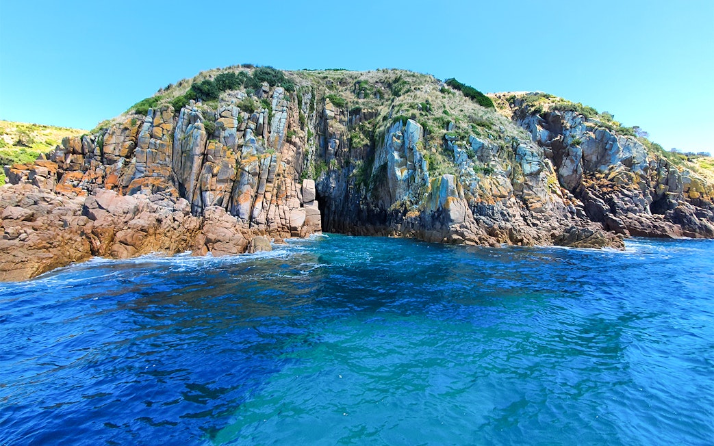Cruise boat near rugged coastal cliffs at Cape Woolamai, Phillip Island.