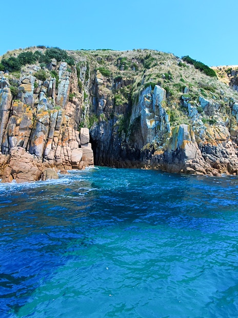 Cruise boat near rugged coastal cliffs at Cape Woolamai, Phillip Island.