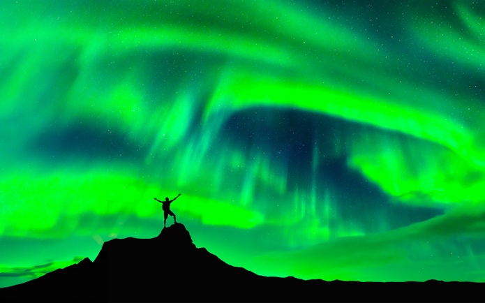 Person standing on a hill under Northern Lights in Rovaniemi, Finland.