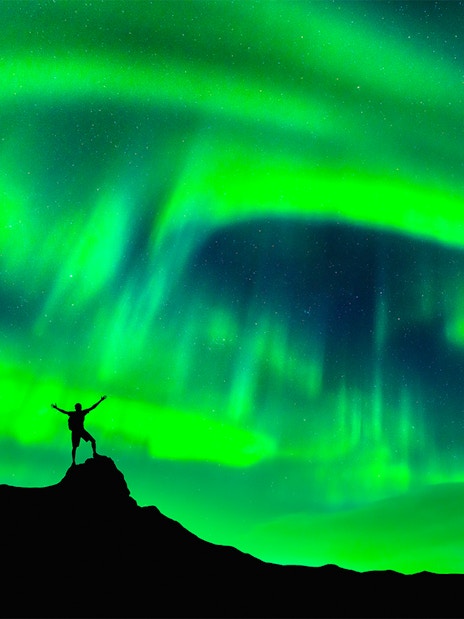 Person standing on a hill under Northern Lights in Rovaniemi, Finland.
