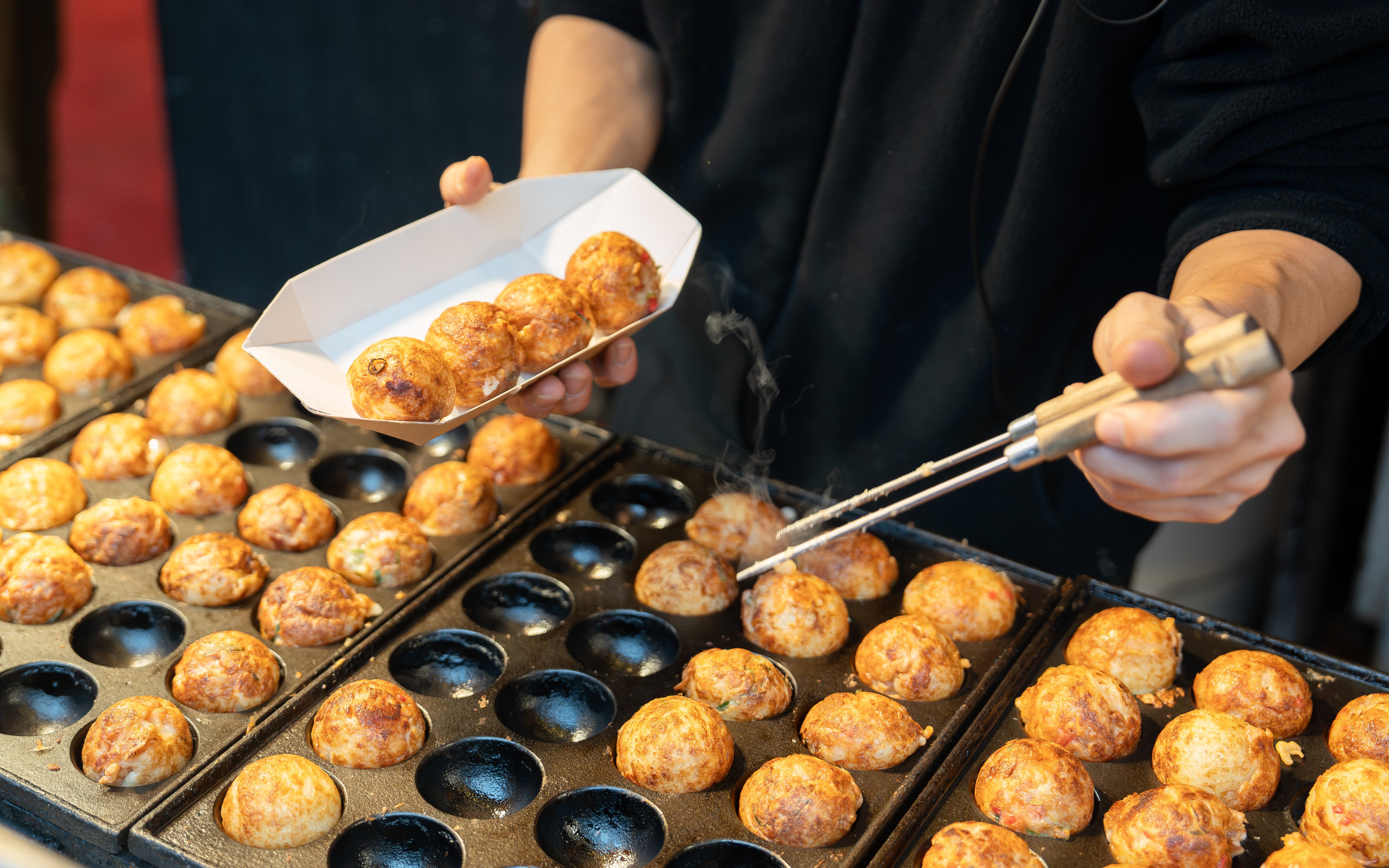 Takoyaki being cooked and served at a street food stall in Japan.