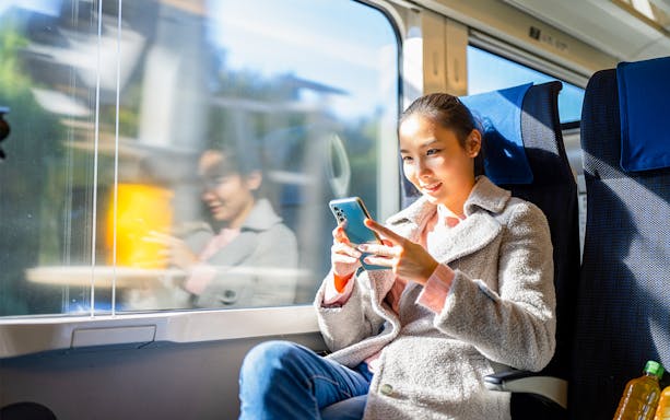 Traveler using smartphone on train in Japan with 3G eSIM card.
