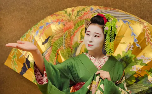 Geisha in traditional green kimono performing with ornate umbrella in Japan.