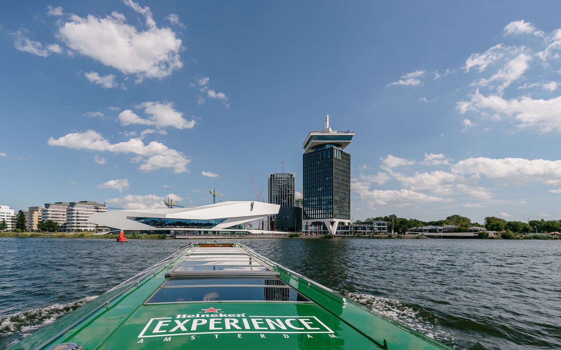 Heineken Canal Cruise boat approaching A'DAM Tower and Eye Film Museum in Amsterdam.