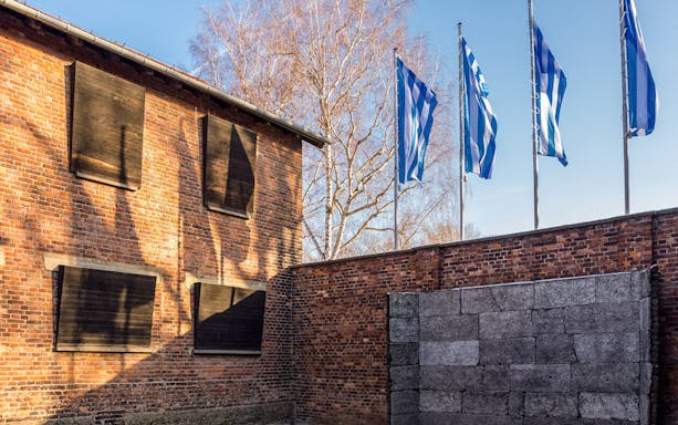 Auschwitz brick building with barred windows and flags, part of Auschwitz & Birkenau tour.
