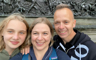 Three people smiling in front of a historic relief sculpture in Glasgow.