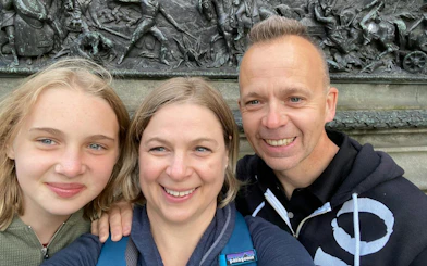 Three people smiling in front of a historic relief sculpture in Glasgow.