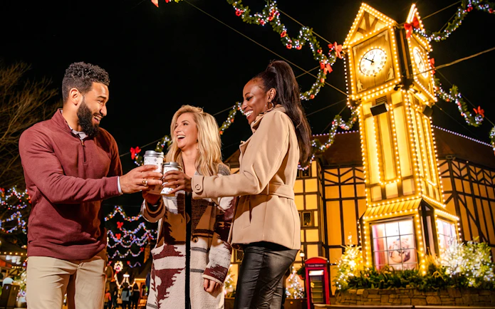 Visitors enjoying hot drinks at Christmas Town, Busch Gardens Williamsburg, with festive lights and clock tower.