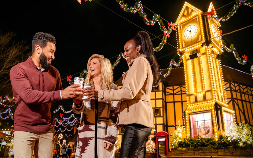 Visitors enjoying hot drinks at Christmas Town, Busch Gardens Williamsburg, with festive lights and clock tower.