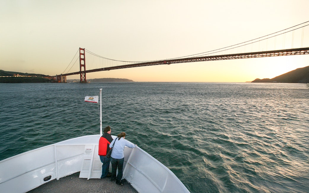 Guests on deck viewing Golden Gate Bridge during California sunset cruise.