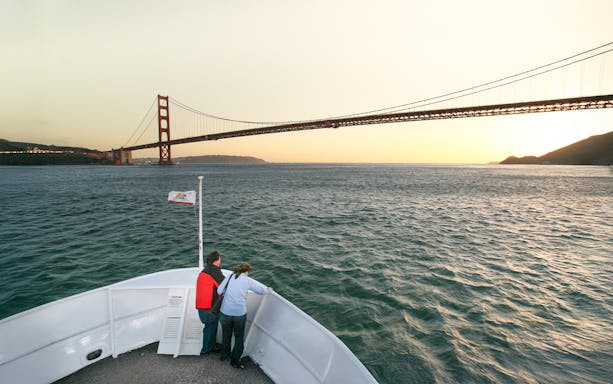 Guests on deck viewing Golden Gate Bridge during California sunset cruise.