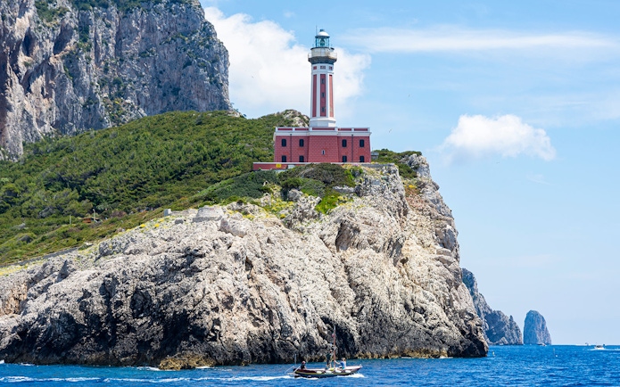 Punta Carena Lighthouse on rocky cliff with boat in Capri, Italy.