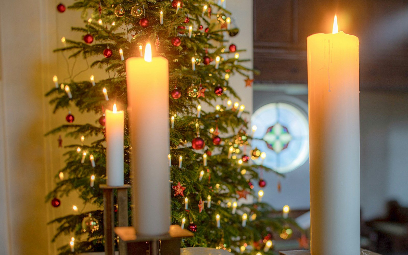 Candles lit in front of a decorated Christmas tree inside a church.