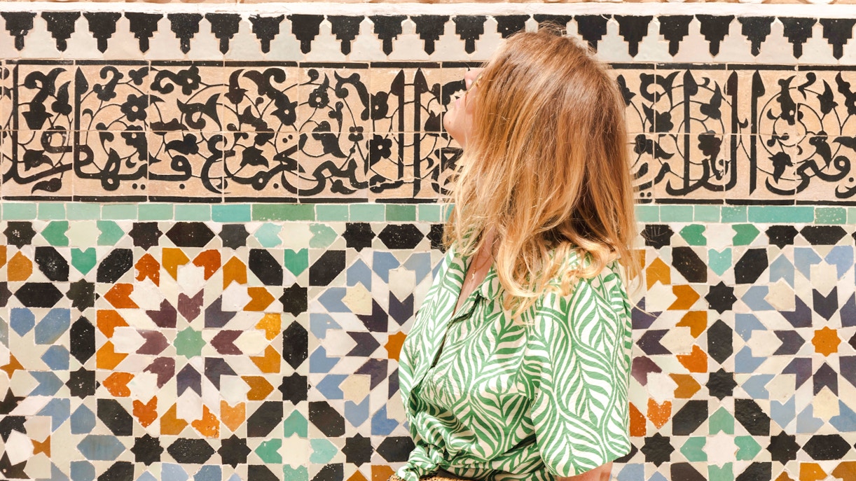 Woman admiring intricate tilework at Ben Youssef, Morocco.