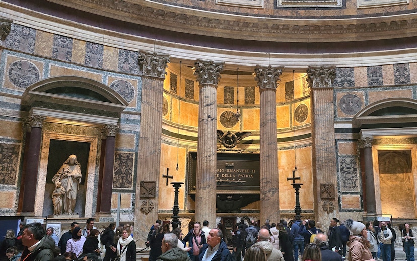Interior view of Rome Pantheon with columns and visitors exploring the historic site.