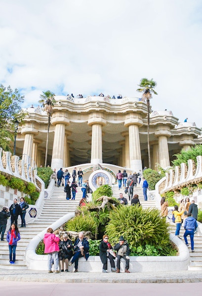 Visitors exploring the iconic staircase and columns of Park Güell in Barcelona.