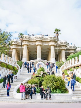 Visitors exploring the iconic staircase and columns of Park Güell in Barcelona.