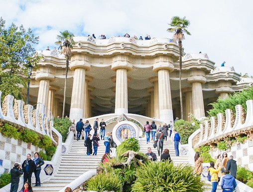 Visitors exploring the iconic staircase and columns of Park Güell in Barcelona.