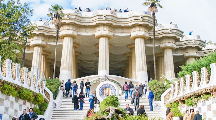 Visitors exploring the iconic staircase and columns of Park Güell in Barcelona.