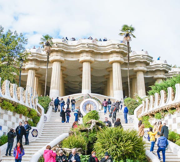 Visitors exploring the iconic staircase and columns of Park Güell in Barcelona.