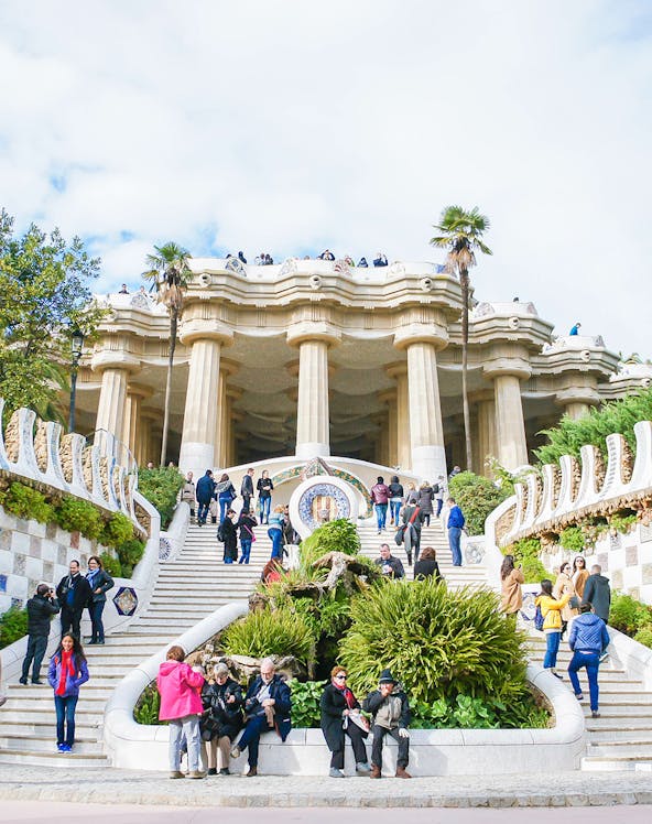 Visitors exploring the iconic staircase and columns of Park Güell in Barcelona.