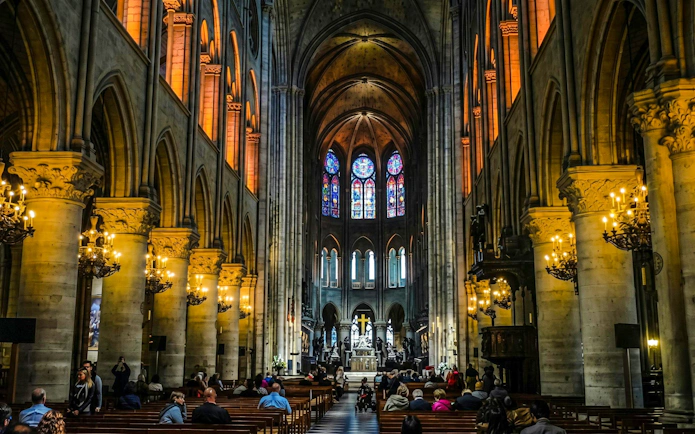 Interior of Notre-Dame Cathedral in Paris with stained glass windows and visitors seated.