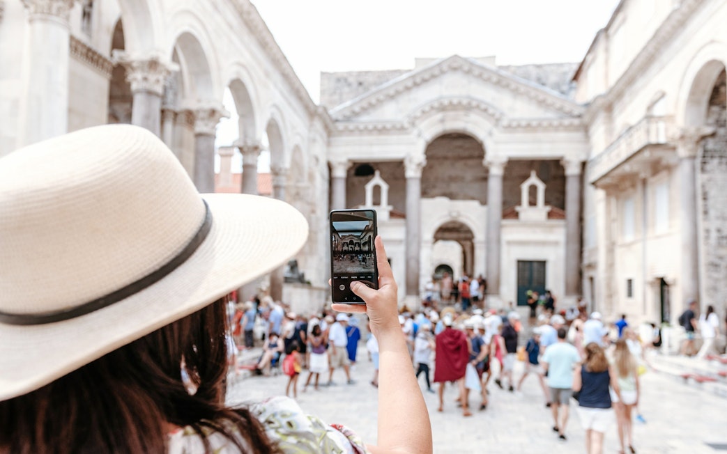 Woman photographing Diocletian's Palace in Split, Croatia, surrounded by tourists.