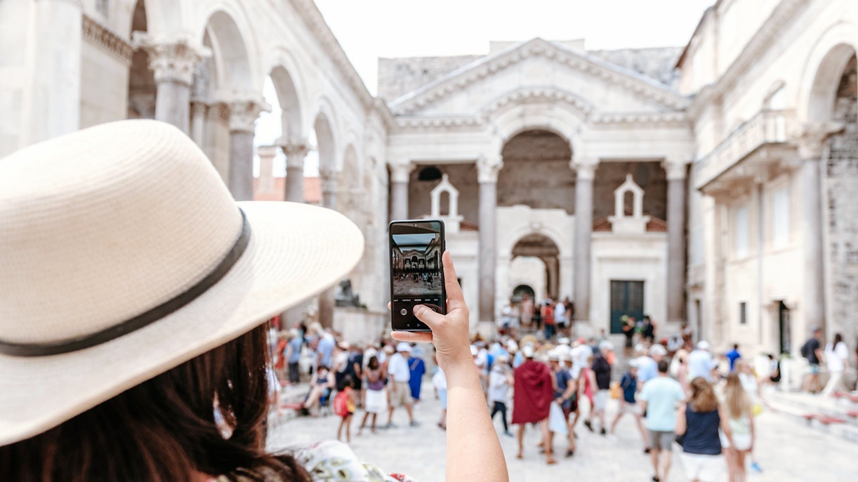 Woman photographing Diocletian's Palace in Split, Croatia, surrounded by tourists.