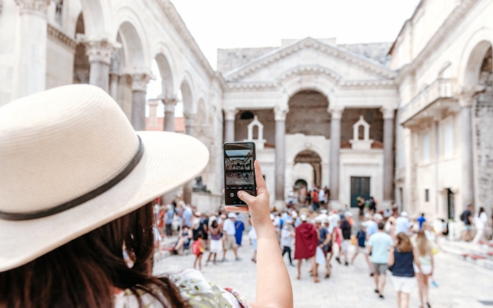 Woman photographing Diocletian's Palace in Split, Croatia, surrounded by tourists.