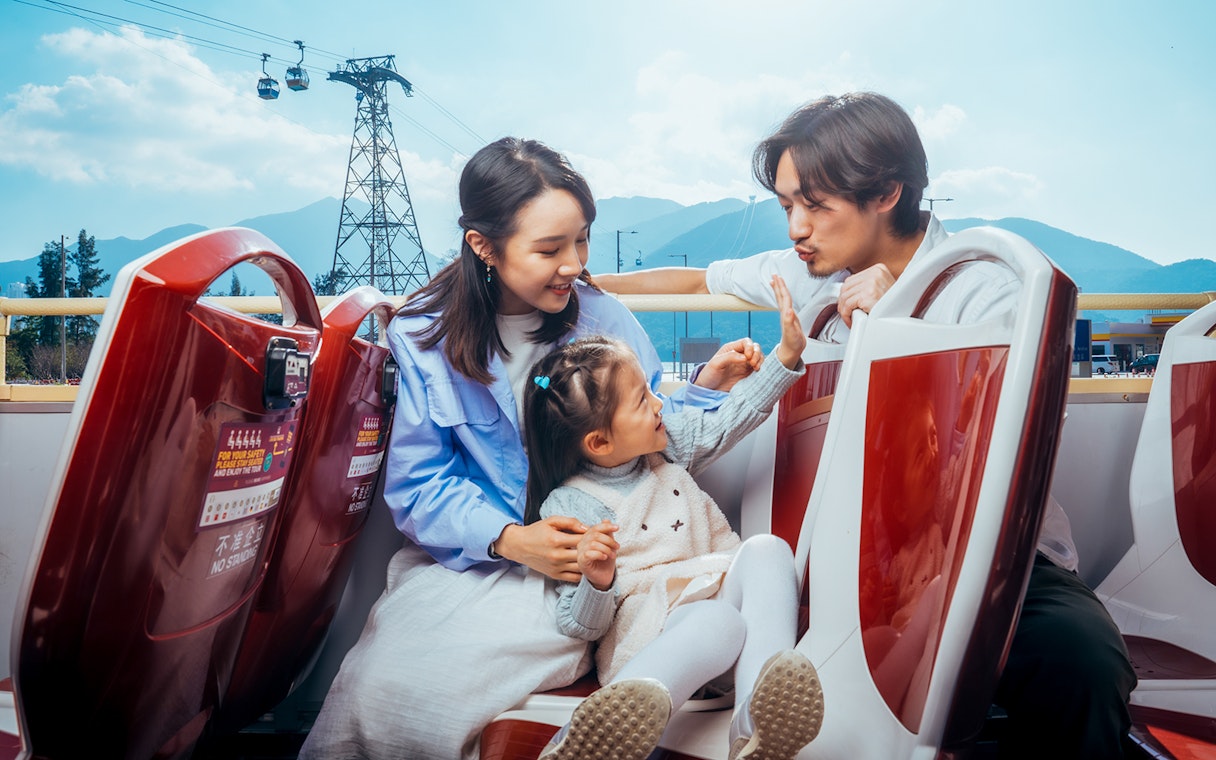 Family enjoying BigBus Lantau Island tour with cable cars and mountains in the background.