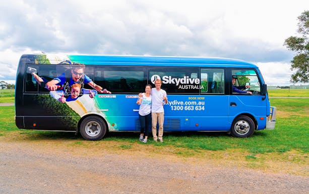 Skydive Airlie Beach bus with skydiving graphic and two people standing beside it.