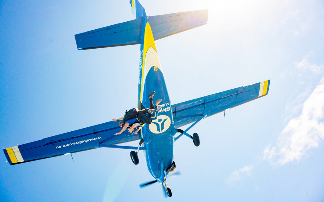 Skydivers jumping from a plane over Melbourne against a clear blue sky.