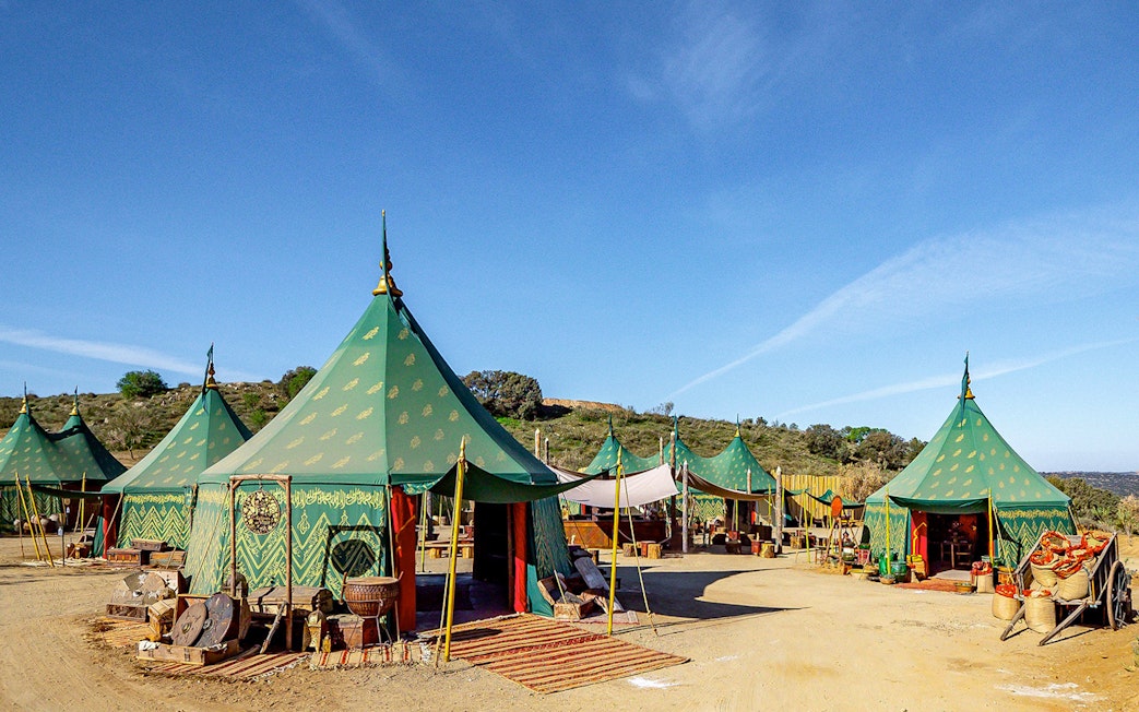 Green medieval tents at Puy du Fou España park, Spain, with rustic decor and clear blue sky.