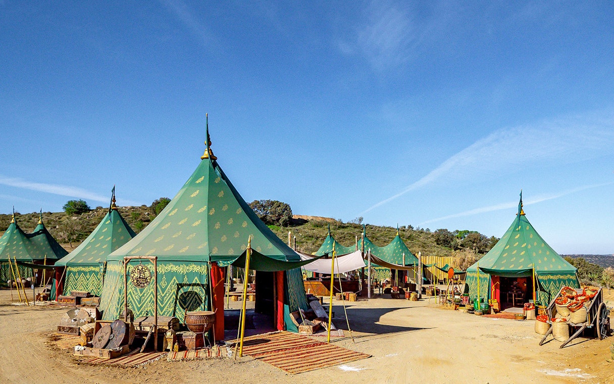 Green medieval tents at Puy du Fou España park, Spain, with rustic decor and clear blue sky.