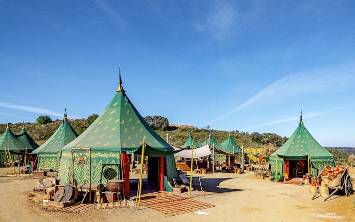 Green medieval tents at Puy du Fou España park, Spain, with rustic decor and clear blue sky.