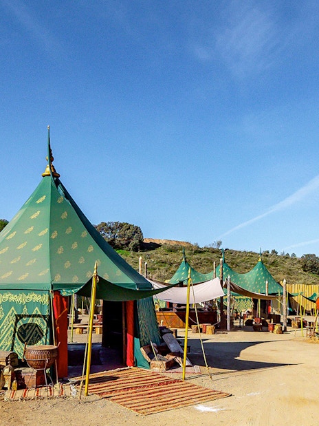 Green medieval tents at Puy du Fou España park, Spain, with rustic decor and clear blue sky.