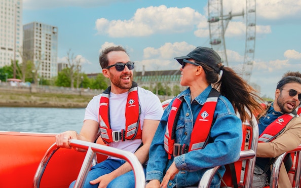 People enjoying a Thames speed boat ride with the London Eye in the background.
