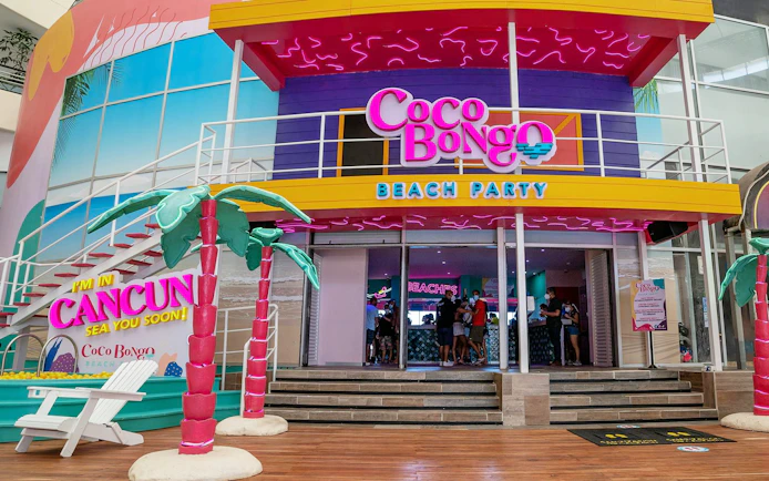 Coco Bongo Beach Party entrance in Cancun with colorful decor and palm tree sculptures.