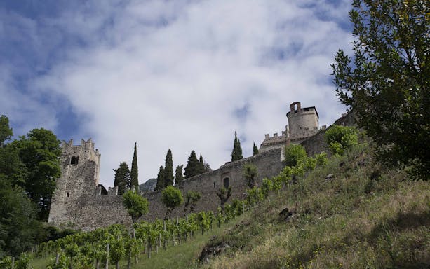 Avio Castle stone walls and towers surrounded by greenery under a cloudy sky.