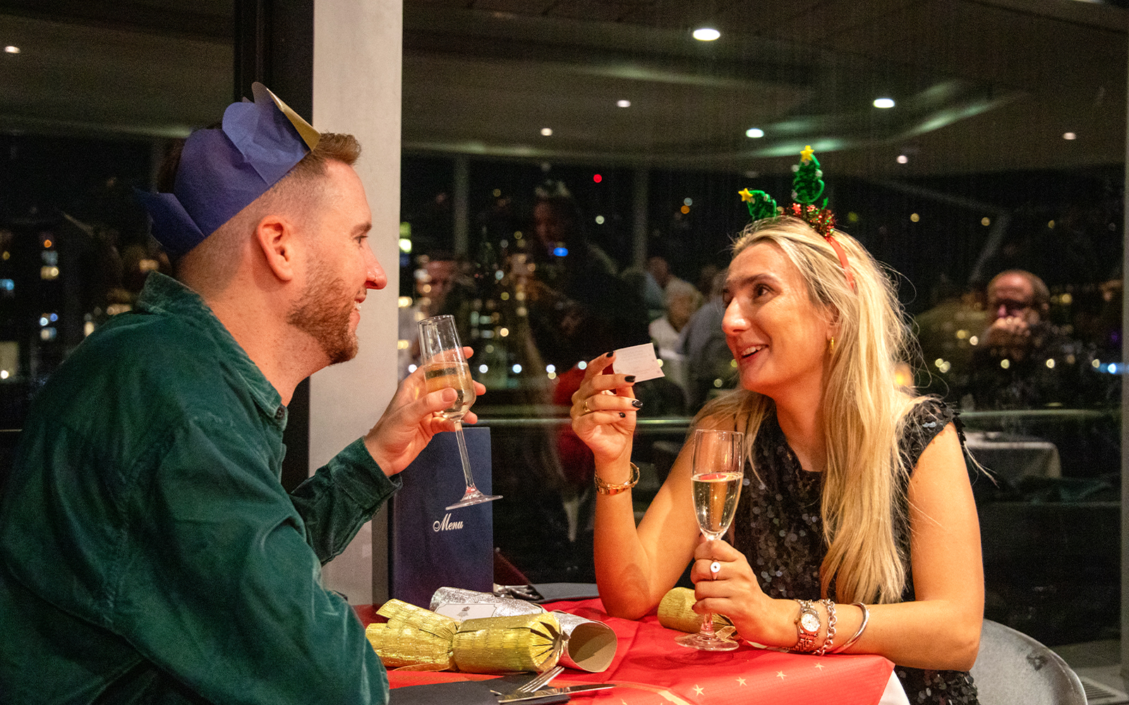 Guests enjoying Christmas dinner on Thames River cruise with festive hats and champagne.