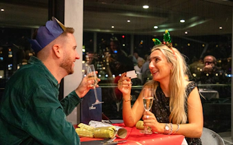 Guests enjoying Christmas dinner on Thames River cruise with festive hats and champagne.