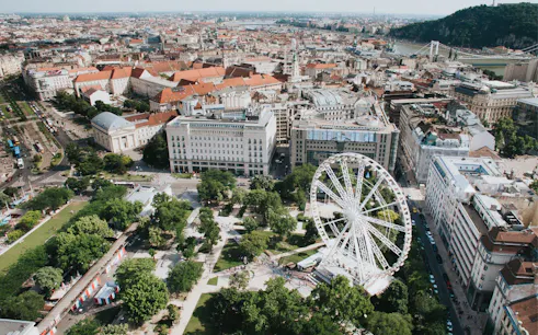 Budapest Eye Ferris wheel in city park with surrounding buildings and river view.