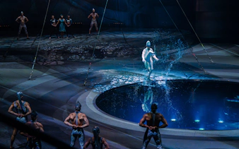 Performer at La Perle show in Dubai walking on water with acrobats in the background.